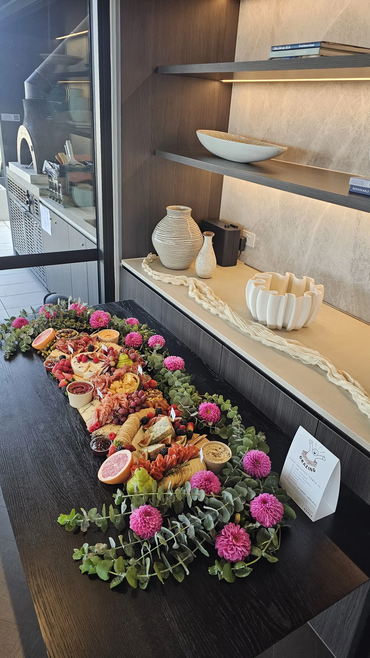 A grazing table runner with cheeses, charcuterie and pink flowers
